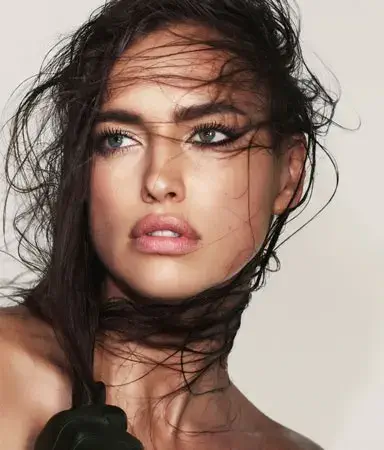 Beauty close-up of a model with wet hair blown across her face, strong eyeliner and luminous skin